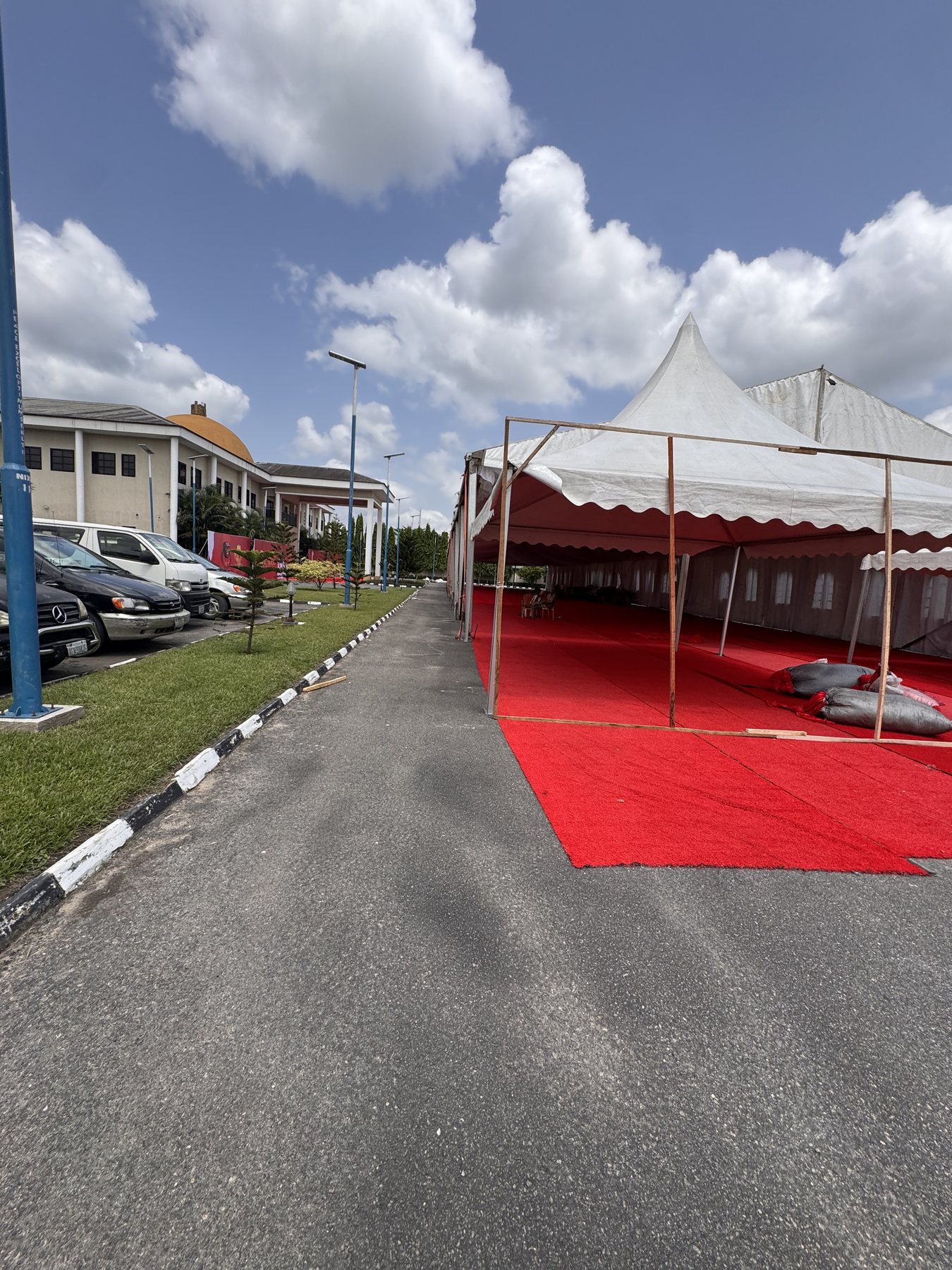 White marquee tents and red carpet laid out along the palace grounds under a blue sky, the palace dome behind.