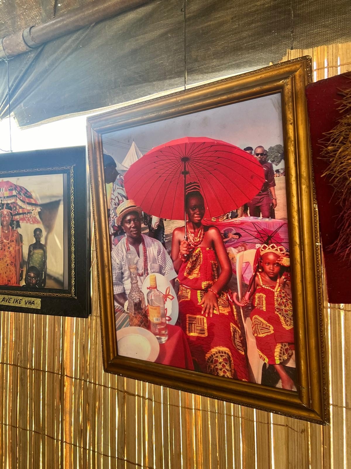 A framed archival photograph of a woman in coral beads under a red ceremonial umbrella.
