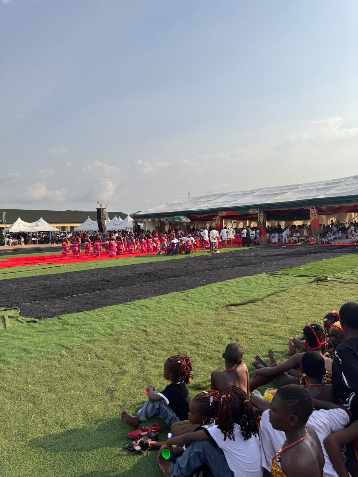 Children sitting on the turf watching dancers in red.